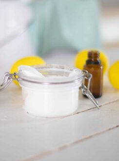 white soft scrub in glass jar on white ship lap, amber essential oil bottle and lemons in background.