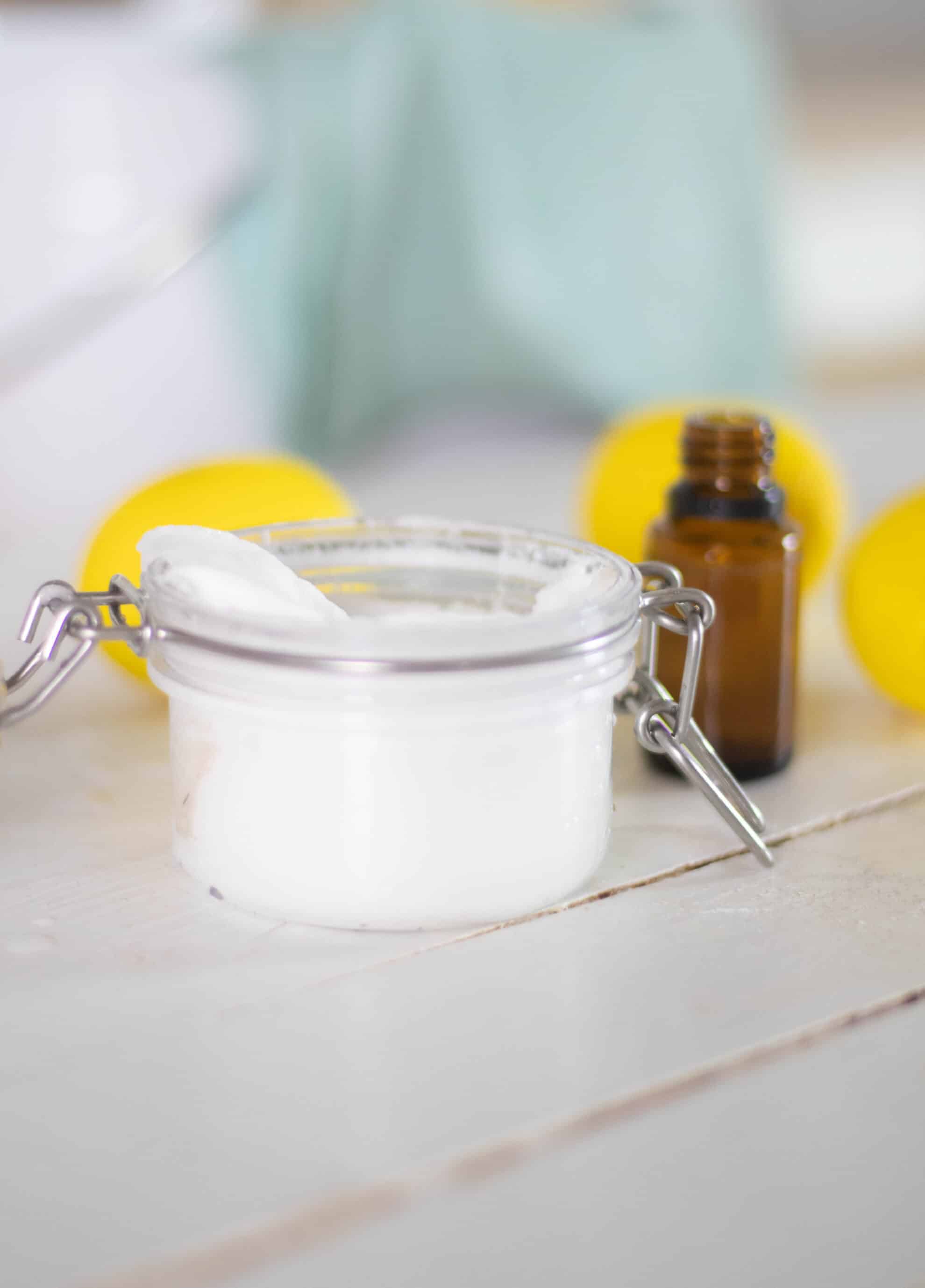 White soft scrub in glass jar on white ship lap with amber essential oil bottle and lemons in background.