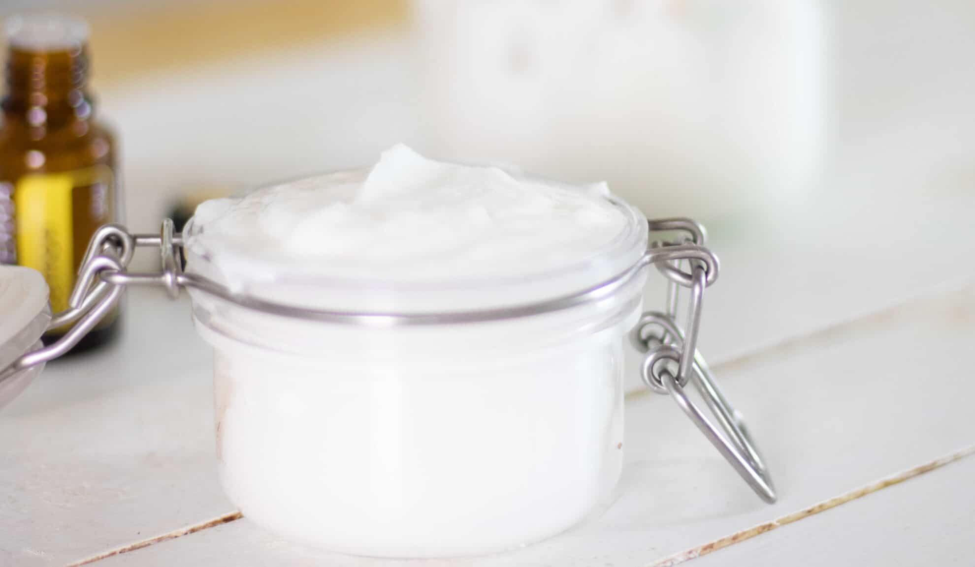 DIY shower cleaner in flip top glass mason jar on table with essential oil bottle in background.