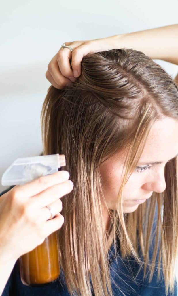 women spraying dry shampoo into her light brown hair