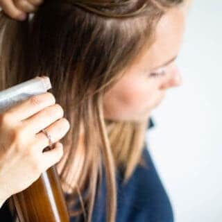 Women applying dry shampoo spray to her hair.