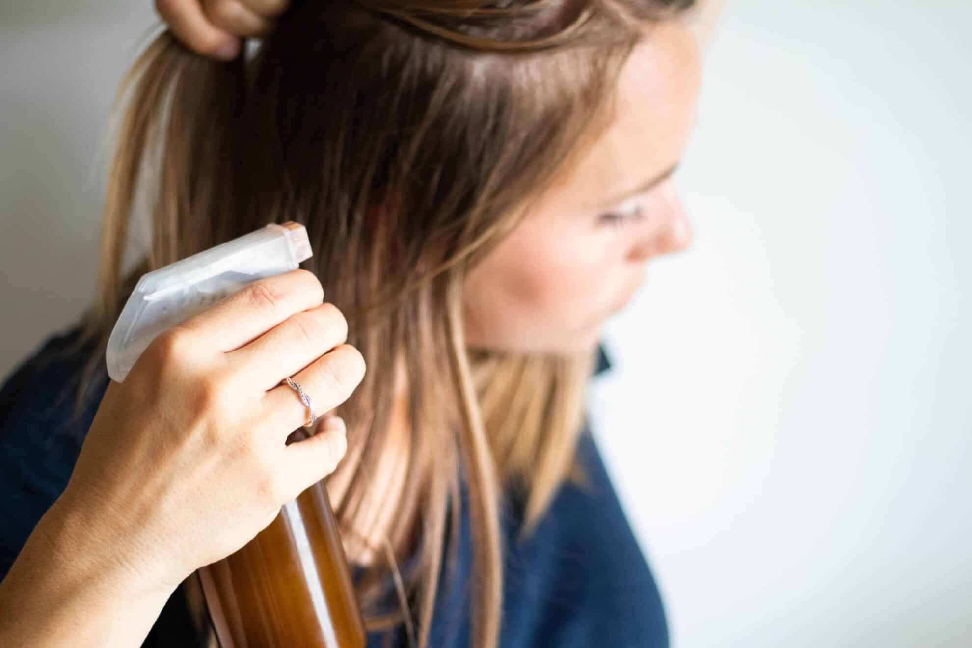 Women applying dry shampoo spray to her hair.