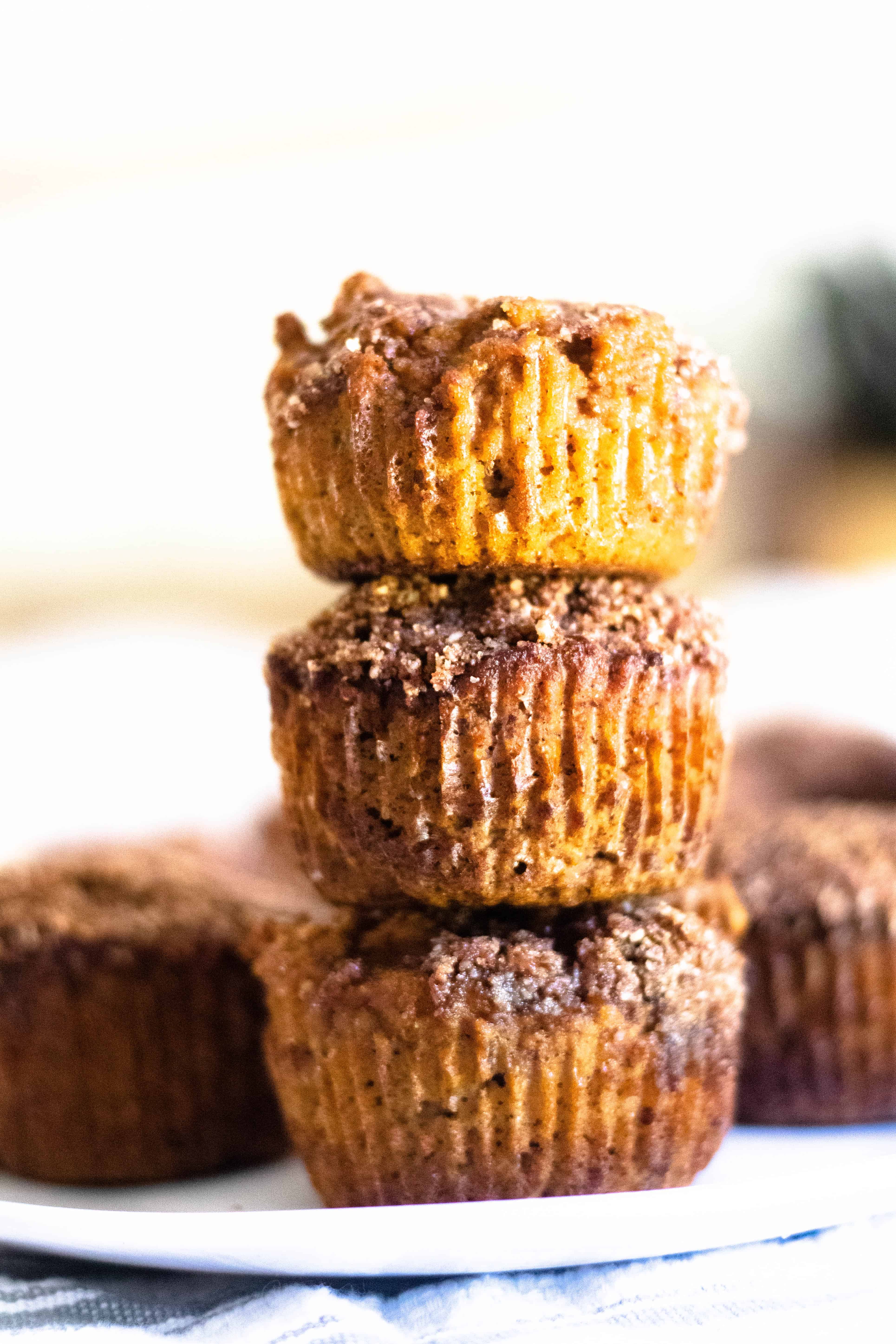 Three pumpkin muffins stacked on top of each other on plate with more muffins in background.