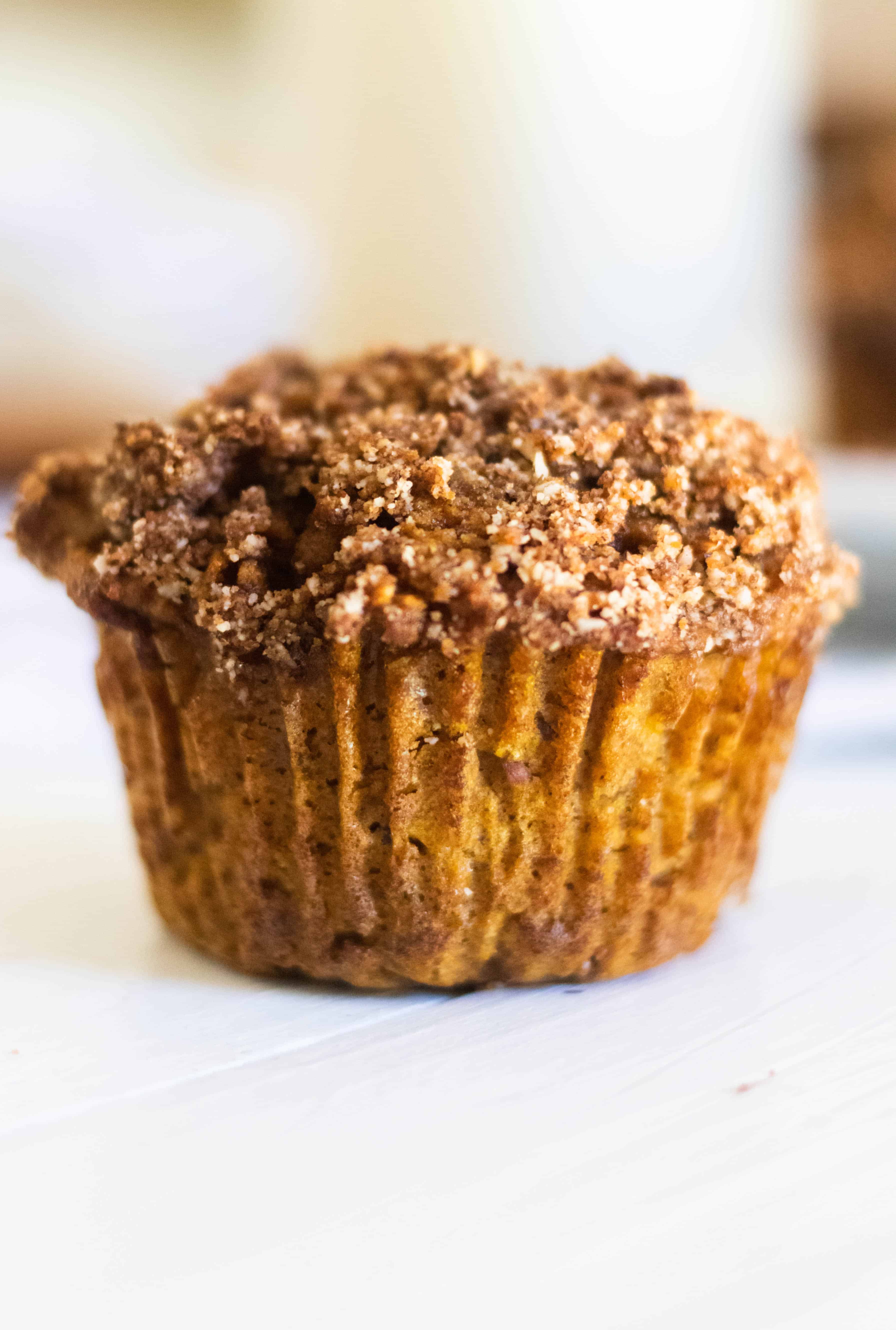 Homemade pumpkin muffin with cinnamon crumble on white table.