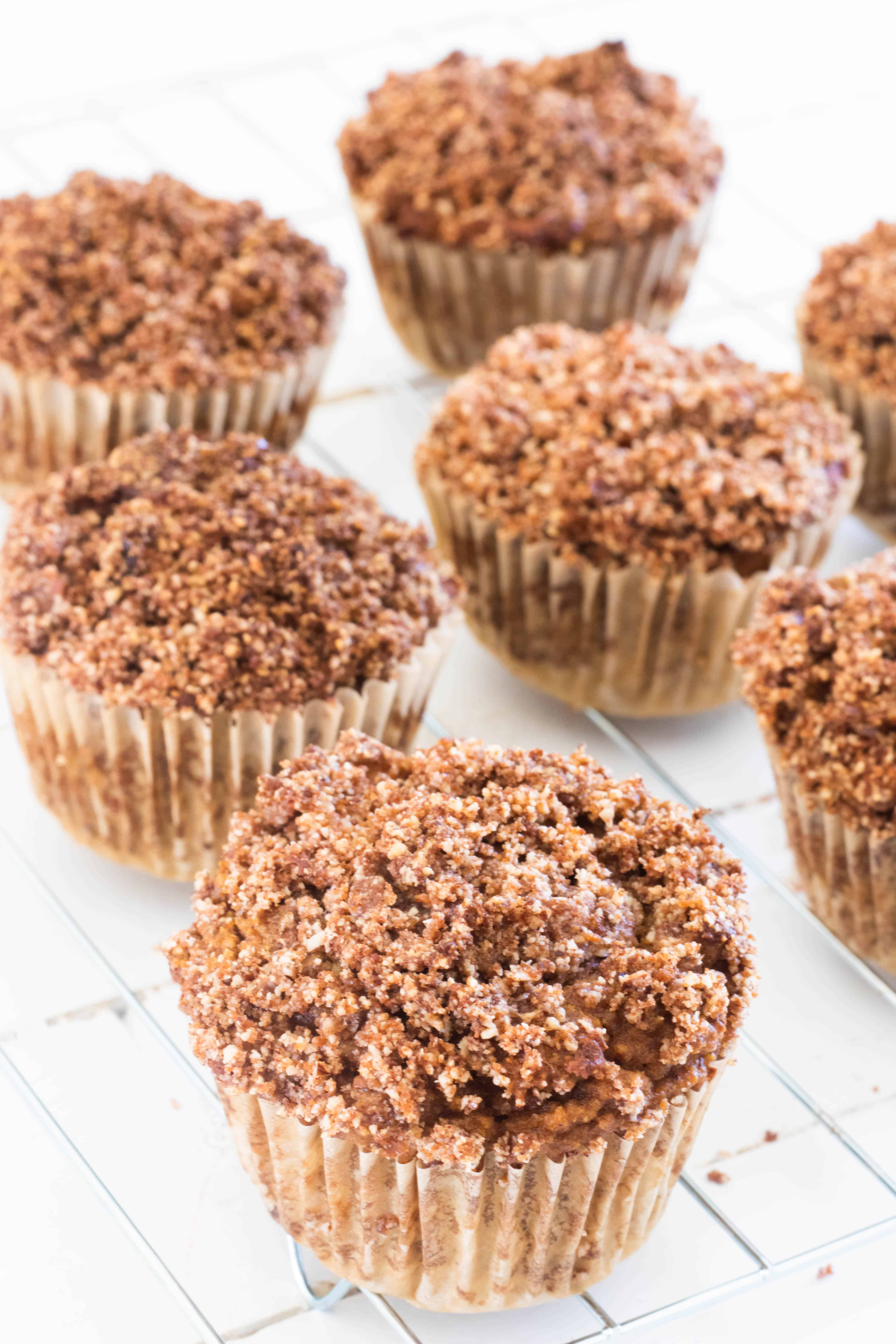 Muffins with crumble topping on drying rack on white table.