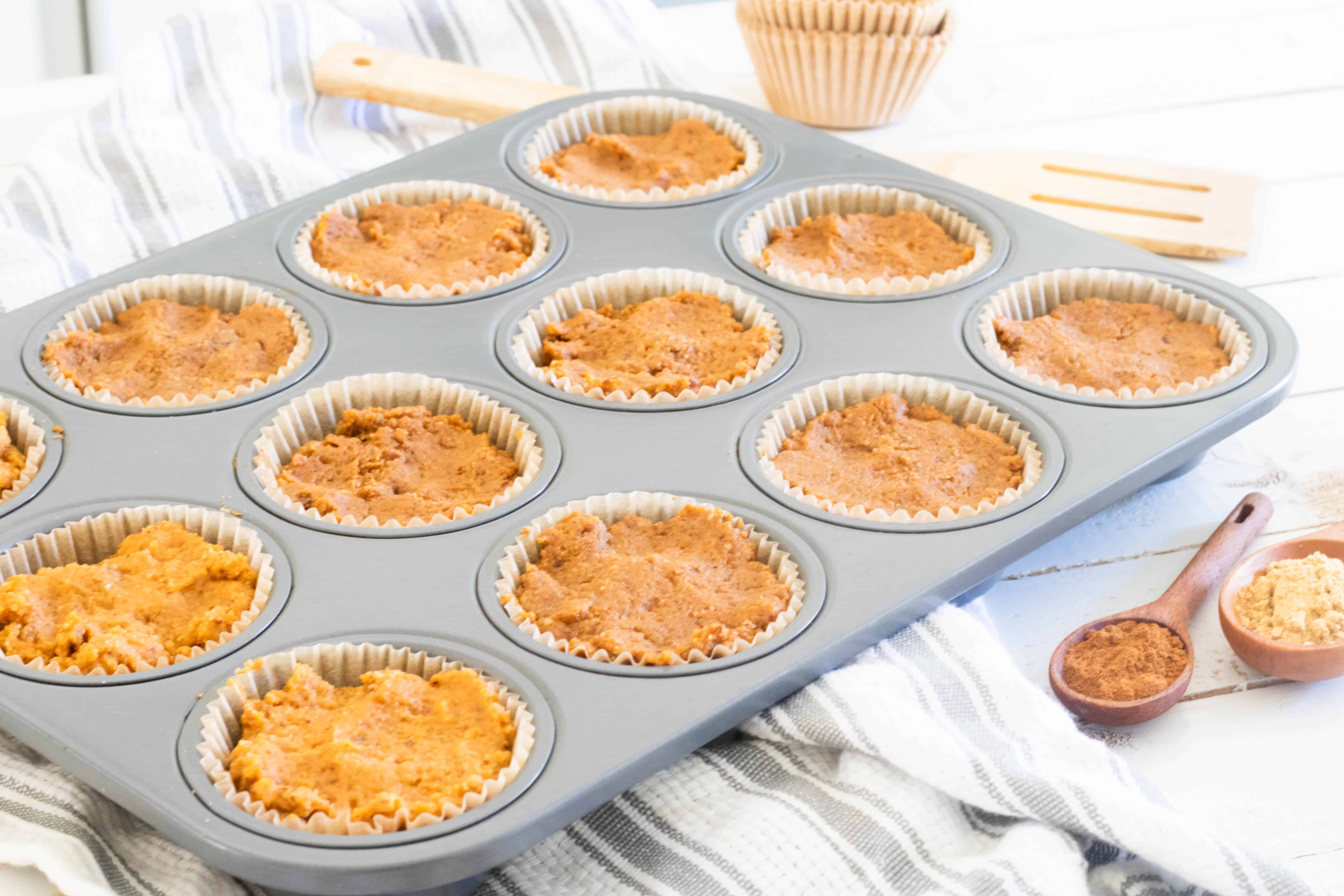 Pumpkin batter in a muffin pan on gray and white strip towel.