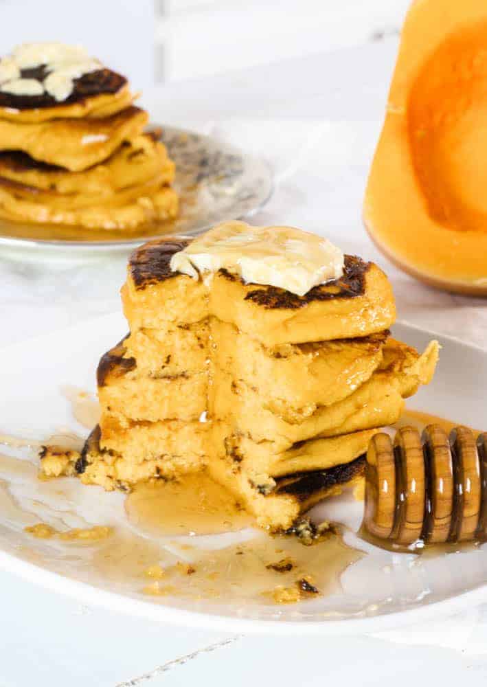 Pumpkin pancakes with butter and honey on white plates.