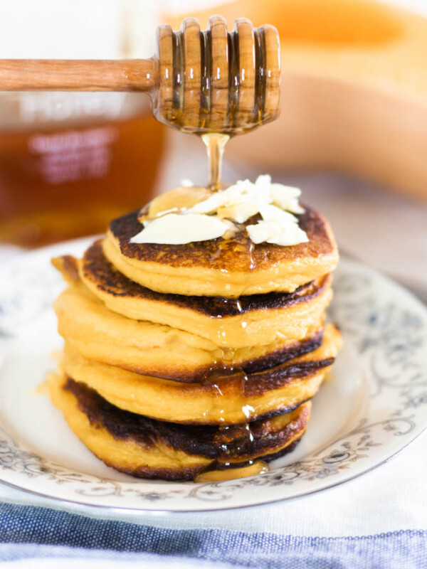 healthy pumpkin pancakes on floral plate with honey being poured over them.