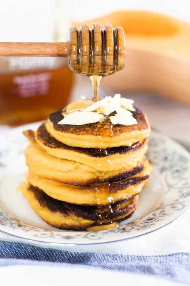Healthy pumpkin pancakes on floral plate with honey being poured over them.