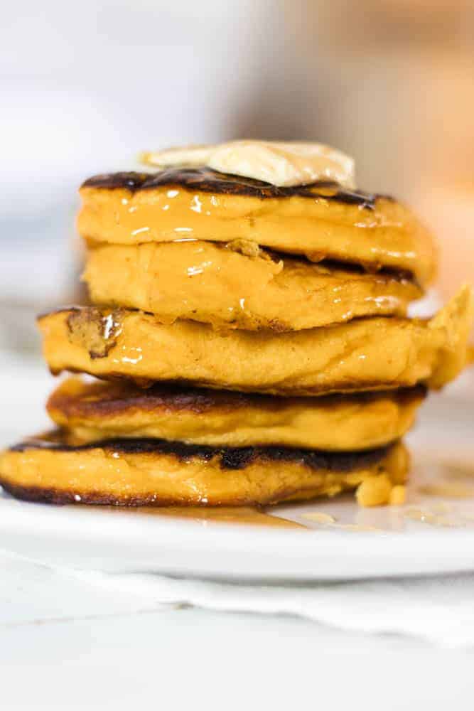 Stack of pumpkin pancakes with butter and honey on top.