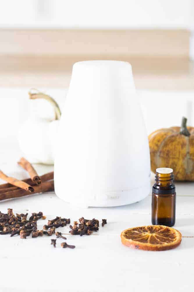 White diffuser surrounded by fall décor on white board.