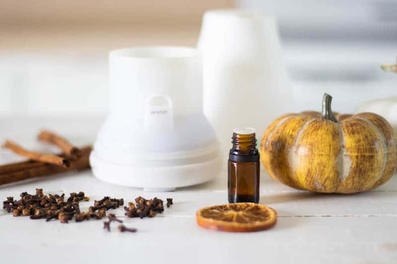 Amber essential oil bottle, oil diffuser, cinnamon sticks, orange slice and cloves buds on table.