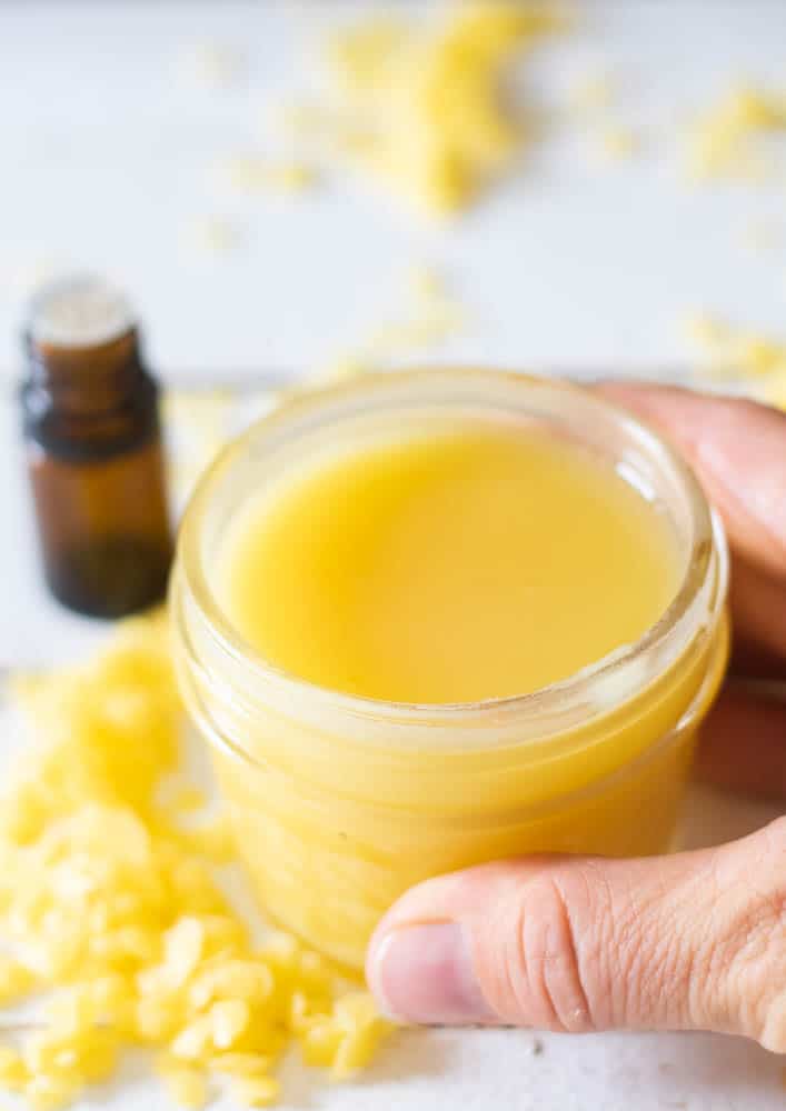 Hand holding mason jar of DIY vapor rub on table with amber colored essential oil bottle.