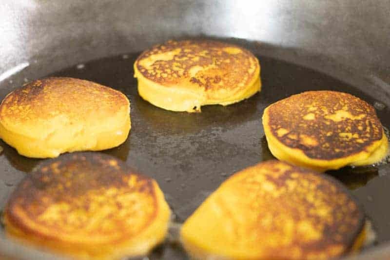 Pancakes frying on cast iron skillet.