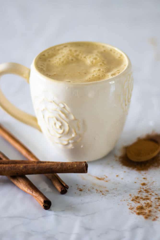 Pumpkin spice latte in white mug on white table with cinnamon sticks.