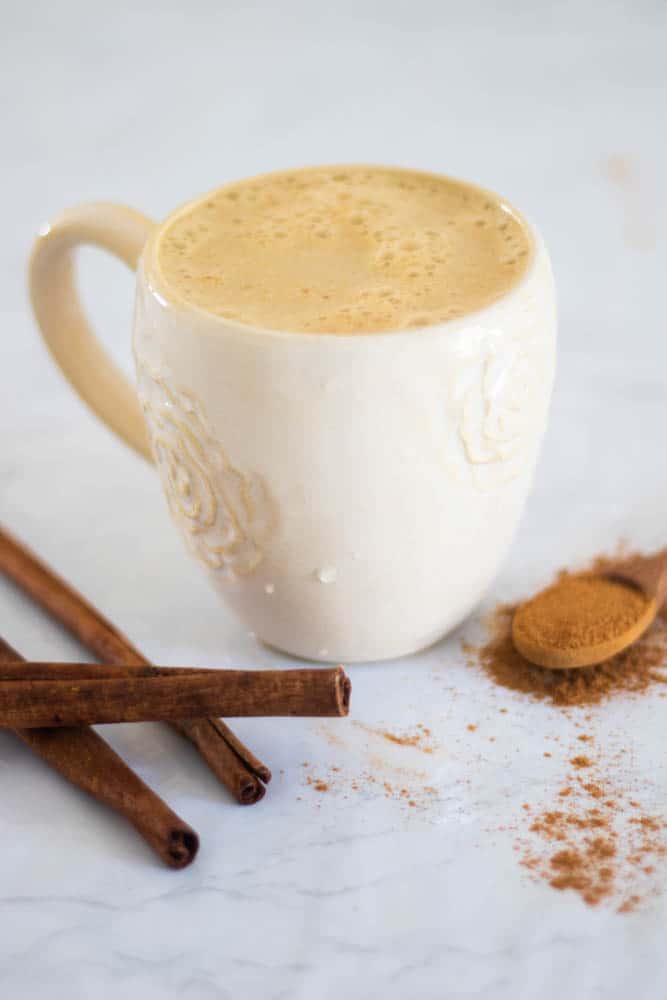 Healthy coffee latte on marble counter with cinnamon sticks and ground cinnamon in wooden spoon.