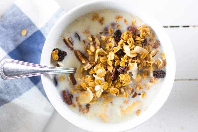 Homemade granola cereal and milk in white bowl on table.