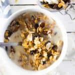 Cereal in milk in white bowl and granola in small jar.