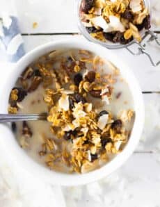 Cereal in milk in white bowl and granola in small jar.
