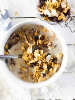 Cereal in milk in white bowl and granola in small jar.