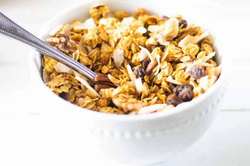 Healthy pumpkin granola in a bowl with spoon on white shiplap.