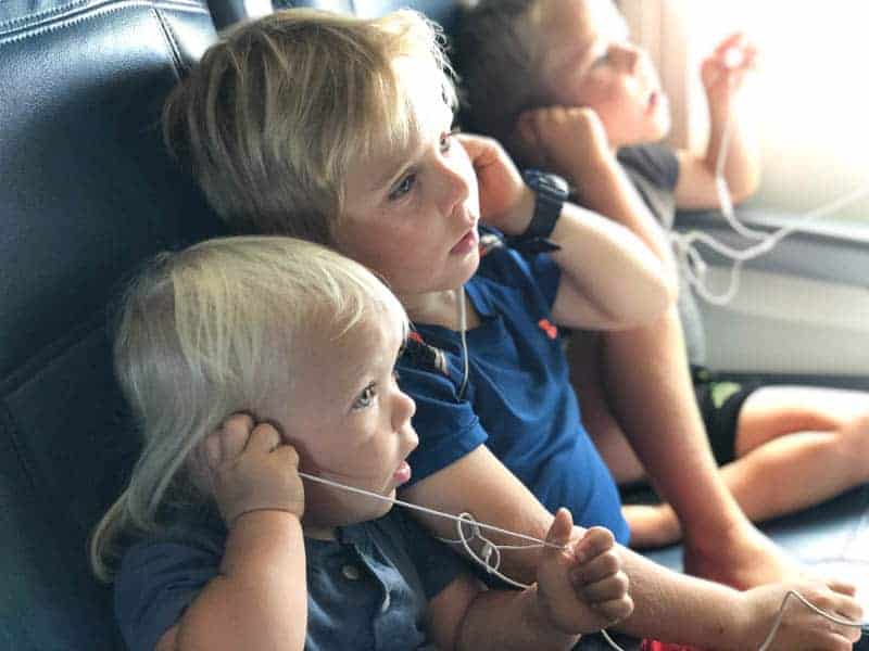 Three little boys sitting in airplane seats with earbuds in.