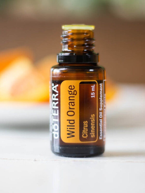 Wild orange essential oil bottle on white table with orange pieces in back