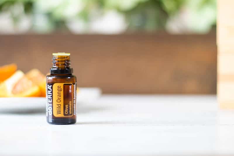 Doterra wild orange bottle on white table with a plate of orange slices in background.