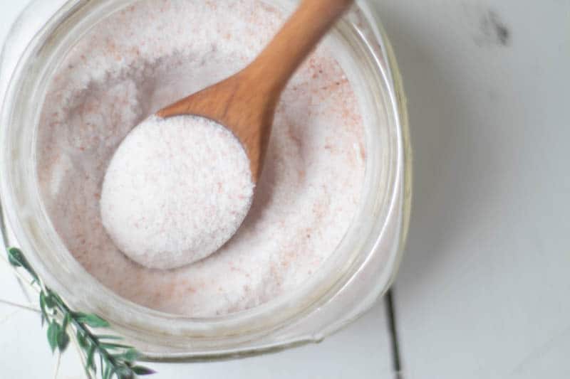 Wooden spoon scooping bath salts from glass container.