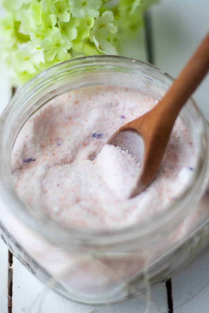 Pink bath salts in wide mouth mason jar with wooden spoon on white shiplap.