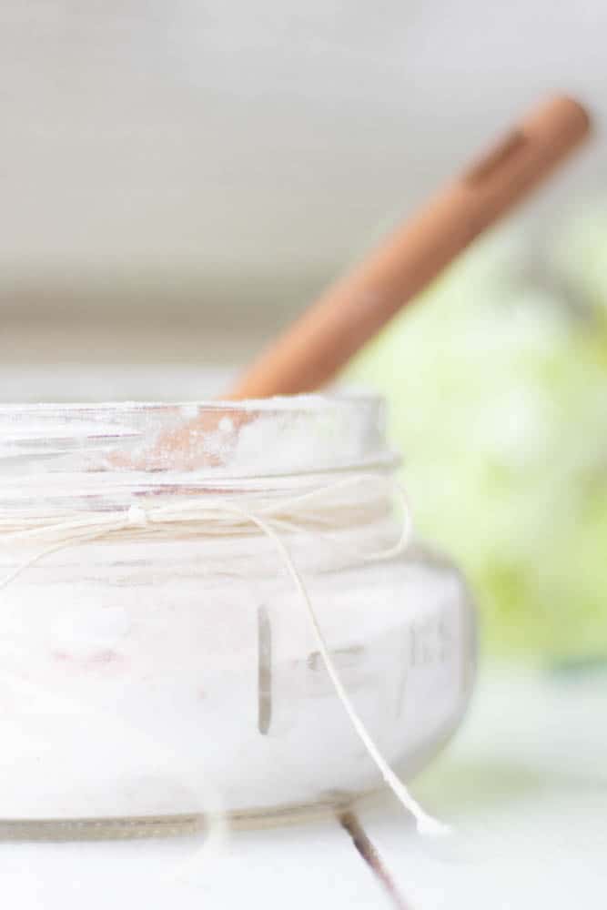 Short glass bowl of fizzing bath salts with wooden spoon.