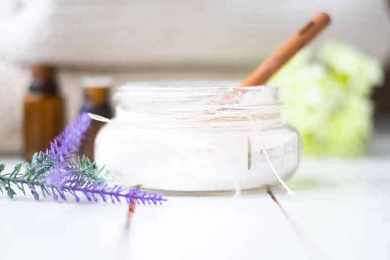 Small mason jar filled with homemade bath salts with lavender sprigs and essential oils in background. 