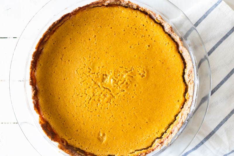 Healthy pumpkin pie in glass pie pan set on white shiplap.