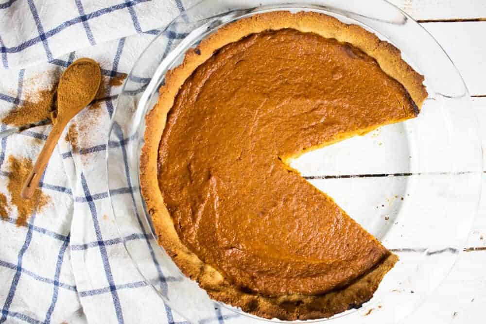 Pumpkin pie with slice cut out of it on blue and white stripe tea towel.