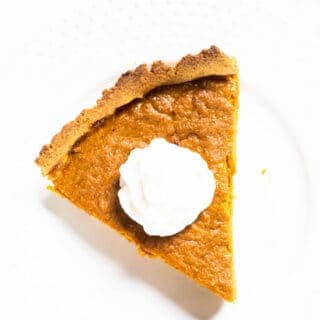 slice of pumpkin pie with whipped cream on white plate