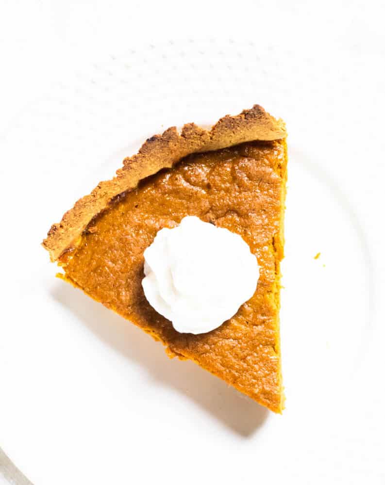 Slice of pumpkin pie with whipped cream on white plate.