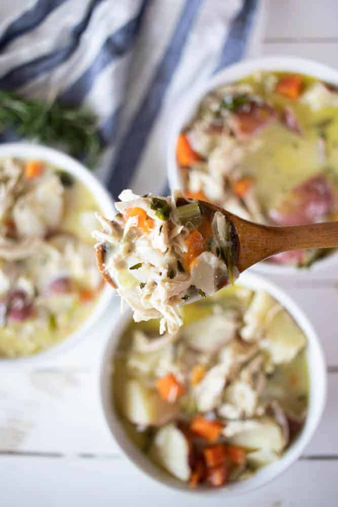 Wooden spoon of creamy chicken soup with bowls of soup in background.