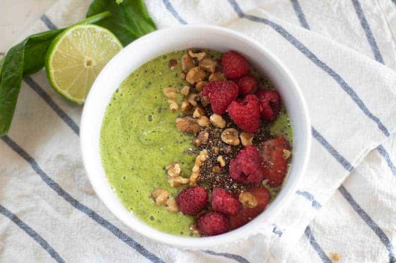 Green smoothie bowl with fresh raspberries and shopped nuts.