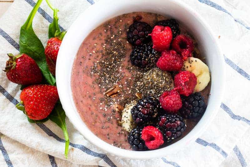 Raspberry smoothie in bowl topped with nuts and chia seeds.