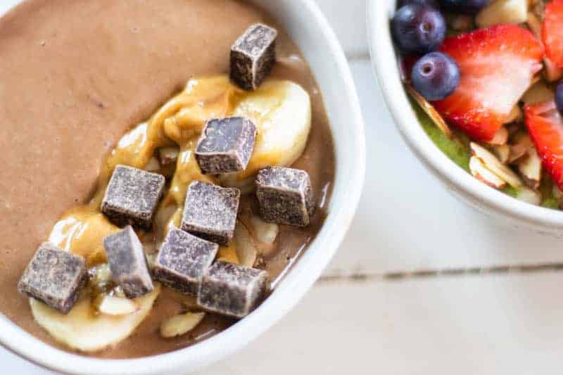 Chocolate smoothie bowl topped with chocolate chunks, banana slices and drizzled with peanut butter.
