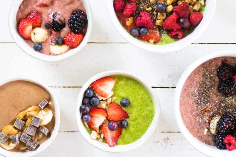 White bowls of different kinds of smoothie bowls on white shiplap.