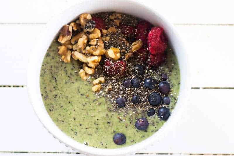 Green smoothie bowl with fresh fruit and chopped nut toppings.