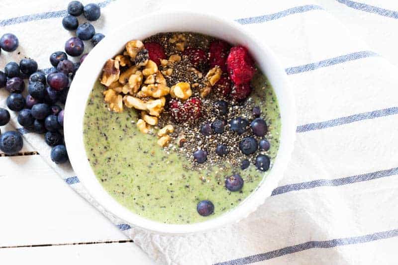 Blueberry smoothie bowl with spinach, walnuts, raspberries, and chia seeds in white bowl.