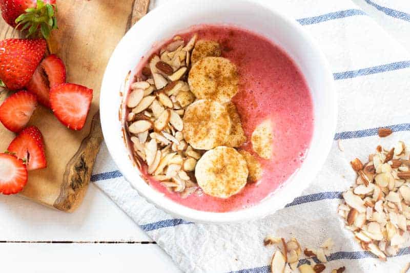 Strawberry banana smoothie bowl topped with sliced banana cinnamon and almonds.