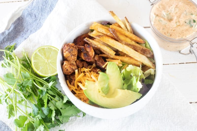 Chicken, fries, and lettuce in white bowl with southwest chipotle ranch dressing mason jar on table.