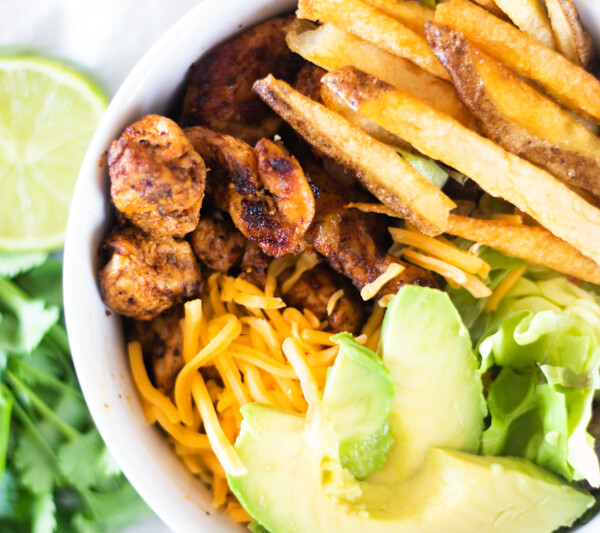 southwest chicken, avocado slices, shredded cheese, and French fries in white bowl