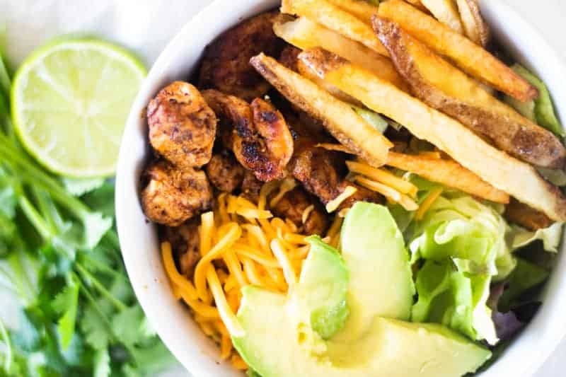 Southwest chicken, avocado slices, shredded cheese, and French fries in white bowl.