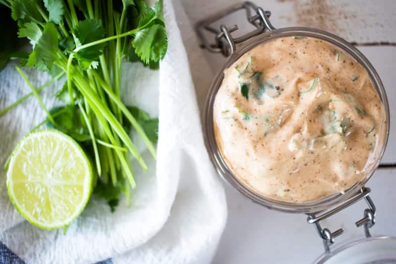 Homemade chipotle ranch dressing in small jar with cilantro and limes in background.