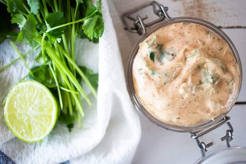 Homemade chipotle dressing in small jar with cilantro and limes on table.