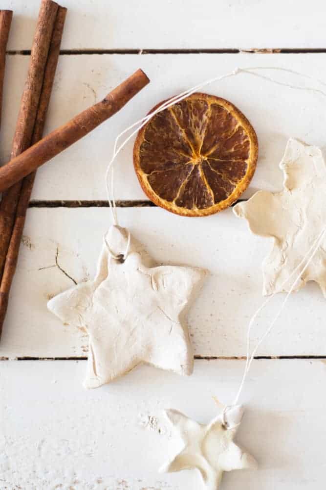 Star clay Christmas ornaments on white ship lap with cinnamon sticks and dried orange slice.